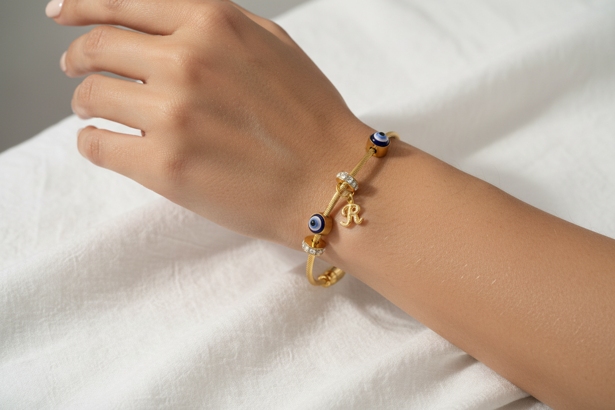 Model wearing gold evil eye bangle with initial charm on wrist